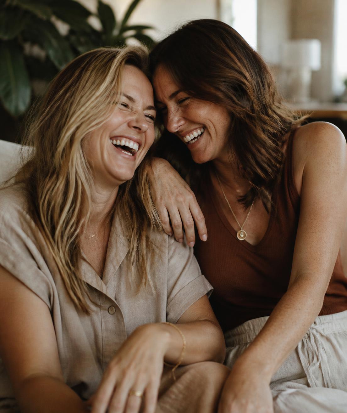 Duas amigas adultas sorrindo juntas em um ambiente iluminado por luz natural